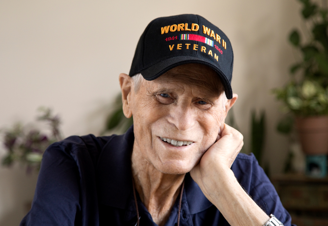 Photo of a World War two veteran wearing a cap and smiling.